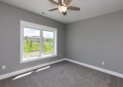 Empty room with gray walls, carpeted floor, a ceiling fan, and a window with a view of the outside neighborhood.