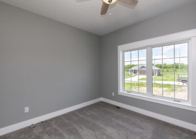 An empty room with gray walls, carpet flooring, and a window with a view of the exterior.