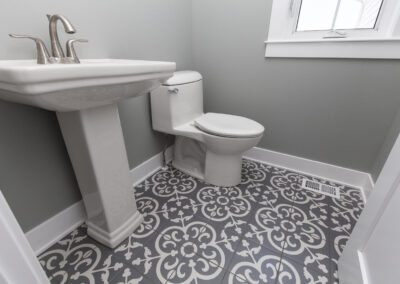 A small bathroom with a pedestal sink, toilet, and decorative tiled floor.