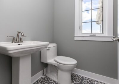 A modern bathroom with a white pedestal sink and toilet beside a window with natural light.