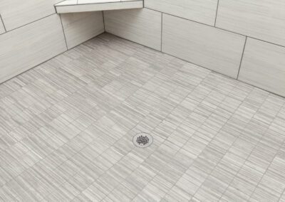 Modern shower with gray tile flooring and built-in bench.