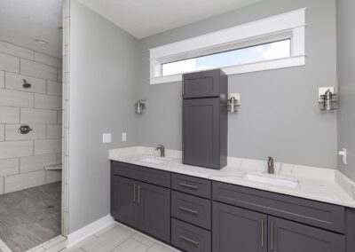 Modern bathroom with dual sinks, dark cabinets, and a walk-in shower.