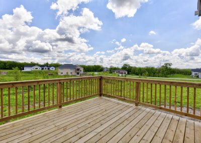 Wooden deck overlooking a suburban landscape with scattered houses and a clear sky with clouds.