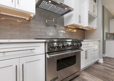 Modern kitchen interior featuring stainless steel appliances, white cabinetry, and a grey subway tile backsplash.